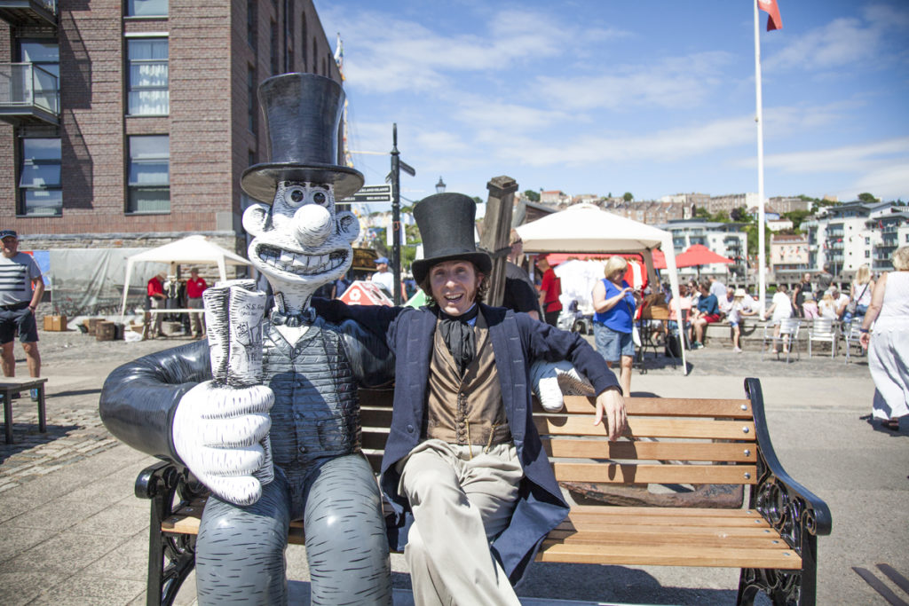 A man in Victorian period dress sitting with a statue on a bench in Bristol Harbour