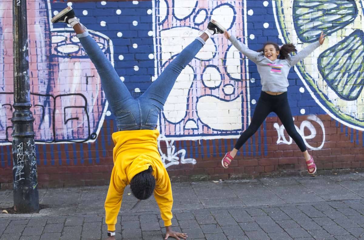 Two people. One leaping in the air, one doing a handstand