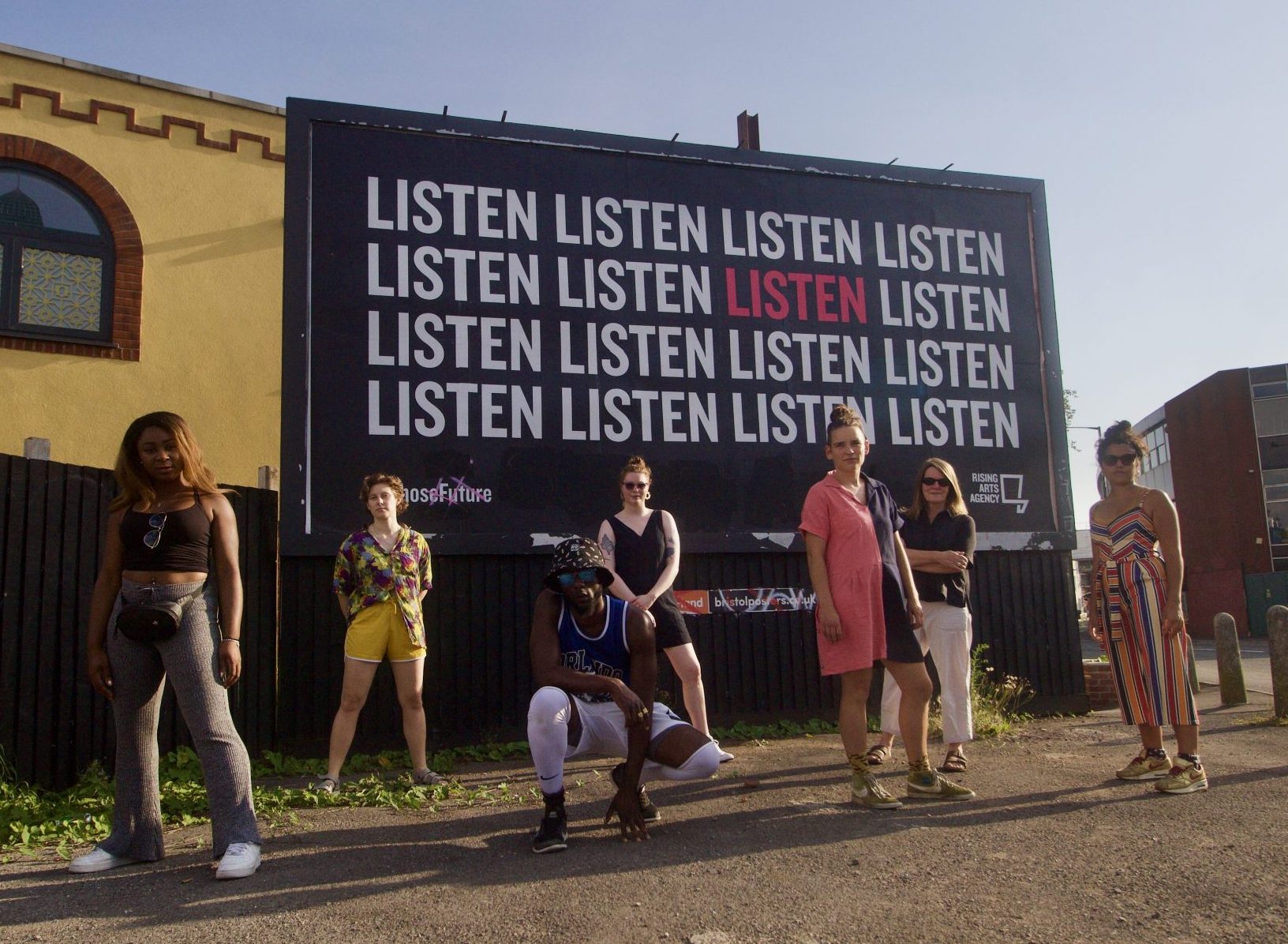 Rising Arts team members in front of a listen banner